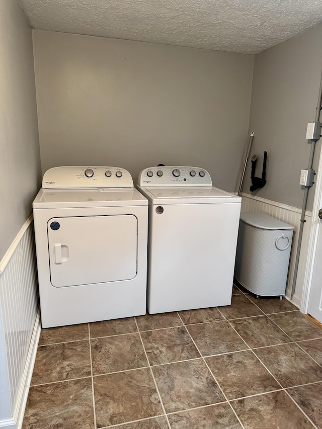 clothes washing area with a wainscoted wall, laundry area, a textured ceiling, and washing machine and clothes dryer