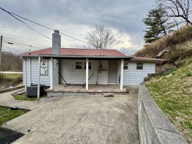 rear view of house featuring metal roof, central AC unit, covered porch, fence, and a chimney