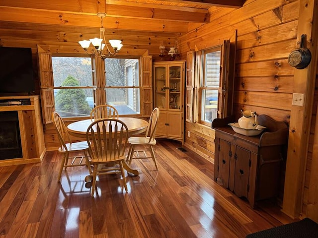 dining space featuring wood walls, a fireplace, wood finished floors, beamed ceiling, and an inviting chandelier