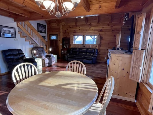 dining area featuring wooden walls, stairway, beamed ceiling, wood finished floors, and an inviting chandelier