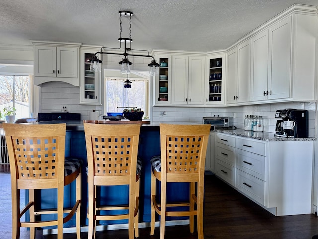 kitchen featuring a textured ceiling, backsplash, dark wood-style floors, glass insert cabinets, and hanging light fixtures