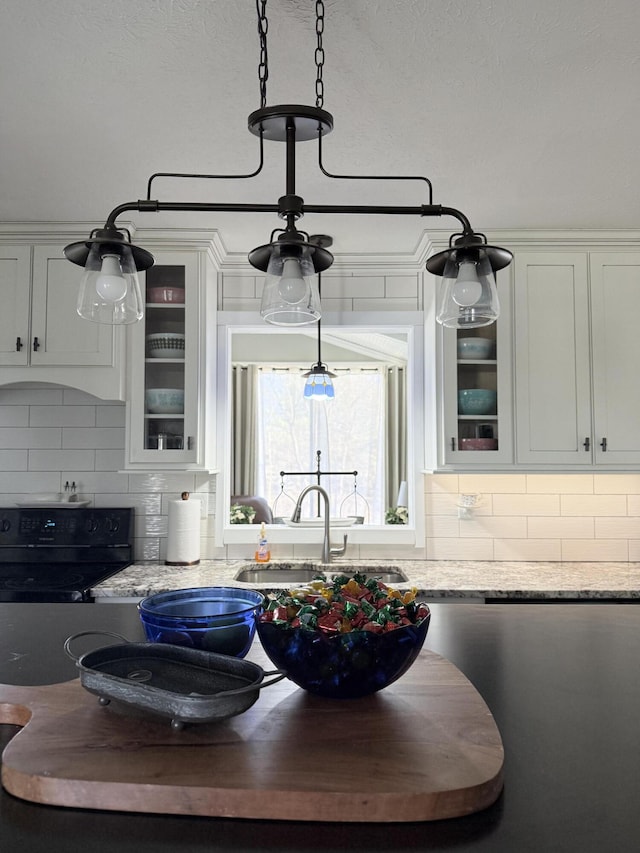 kitchen with black / electric stove, a sink, decorative backsplash, white cabinets, and glass insert cabinets