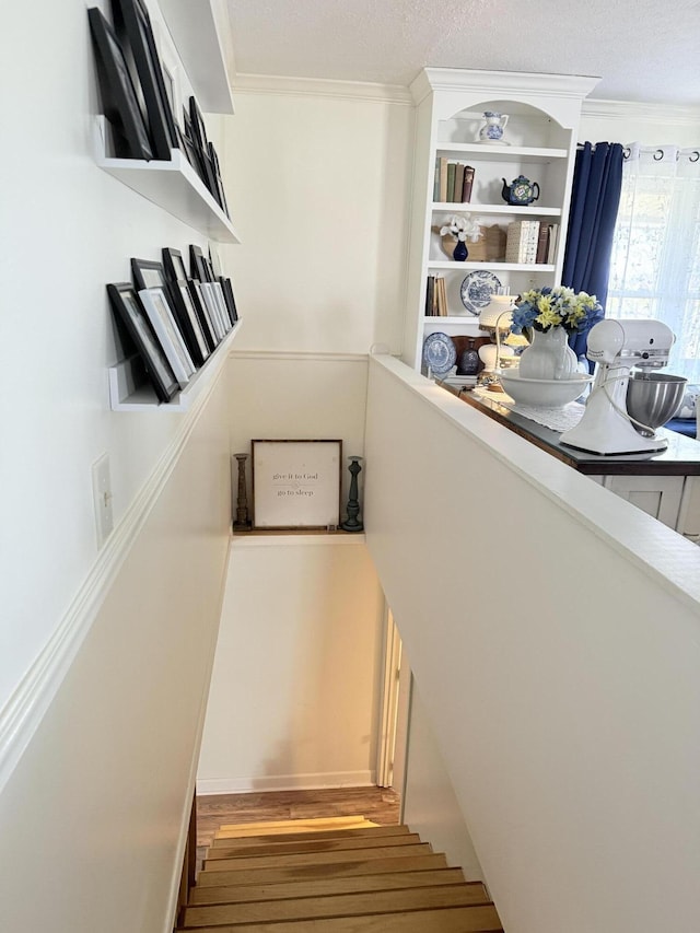 staircase with a textured ceiling, crown molding, and wood finished floors