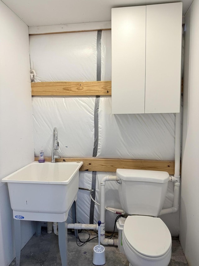 bathroom with toilet, concrete flooring, and a sink