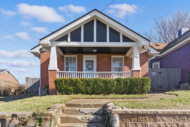 view of front of property with covered porch, brick siding, and fence