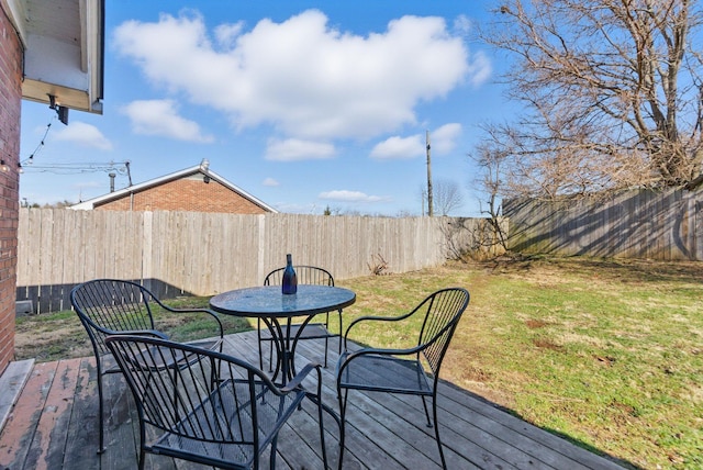 deck with outdoor dining area, a fenced backyard, and a lawn