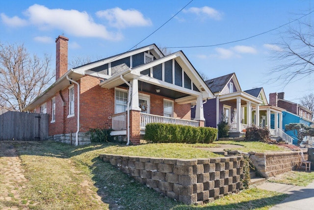 view of front facade with covered porch, brick siding, a chimney, and fence