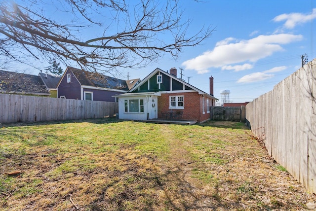 rear view of property with a yard, brick siding, a chimney, and a fenced backyard