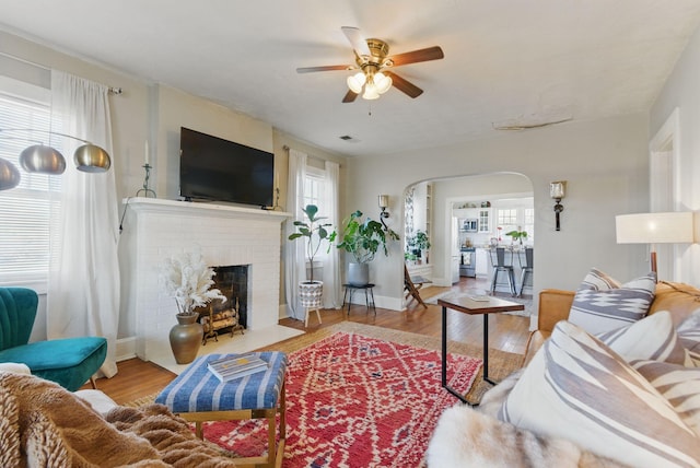 living area featuring arched walkways, a fireplace, wood finished floors, and a healthy amount of sunlight