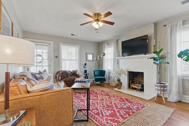 living area with a fireplace, wood finished floors, visible vents, and a healthy amount of sunlight