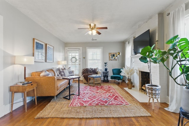 living area with ceiling fan, a fireplace, and wood finished floors