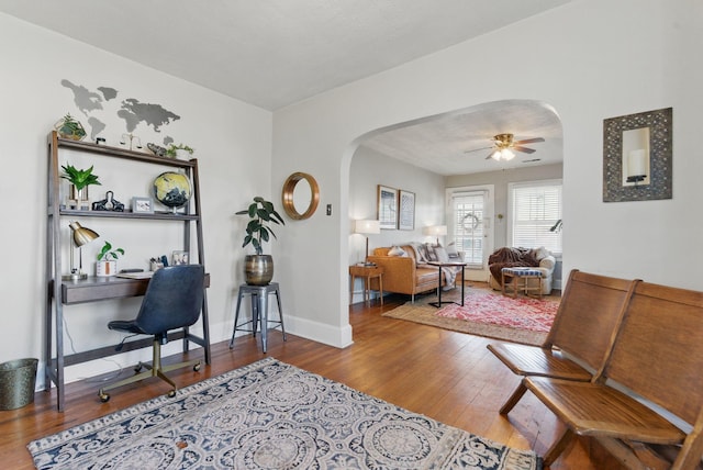office featuring a ceiling fan, arched walkways, wood-type flooring, and baseboards