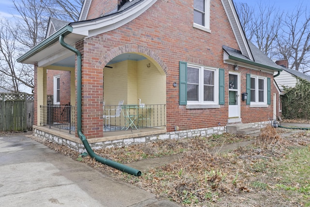 view of home's exterior featuring covered porch, roof with shingles, fence, and brick siding