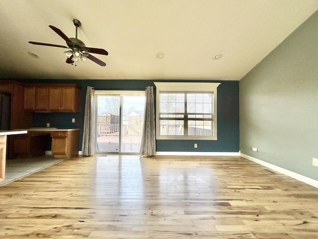 interior space with light wood finished floors, lofted ceiling, a ceiling fan, brown cabinetry, and baseboards