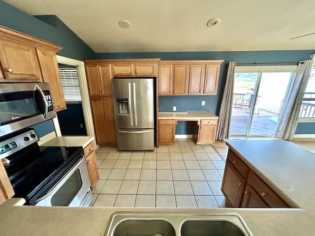 kitchen featuring light tile patterned floors, lofted ceiling, stainless steel appliances, light countertops, and built in desk