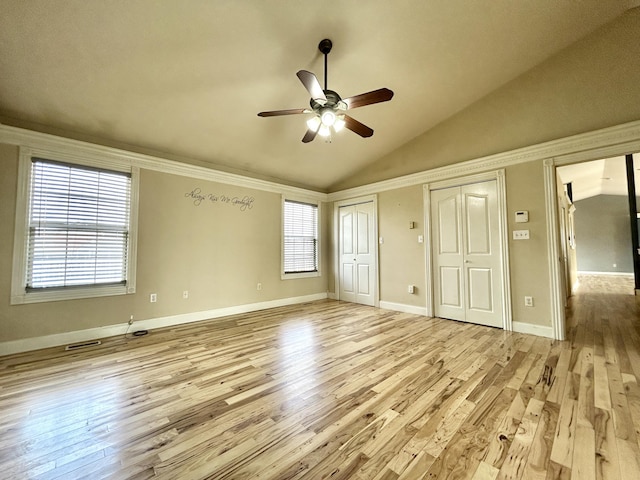 unfurnished bedroom with light wood-style floors, vaulted ceiling, and two closets