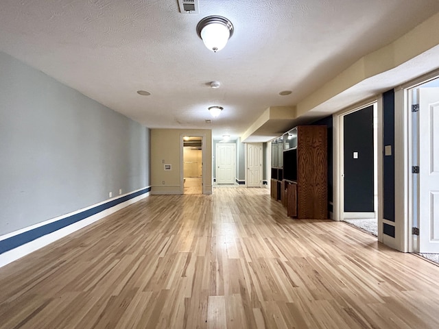 unfurnished living room featuring light wood-type flooring, visible vents, a textured ceiling, and baseboards