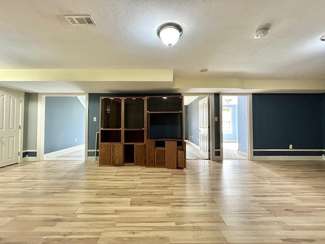 unfurnished living room with baseboards, visible vents, light wood-style flooring, and a textured ceiling