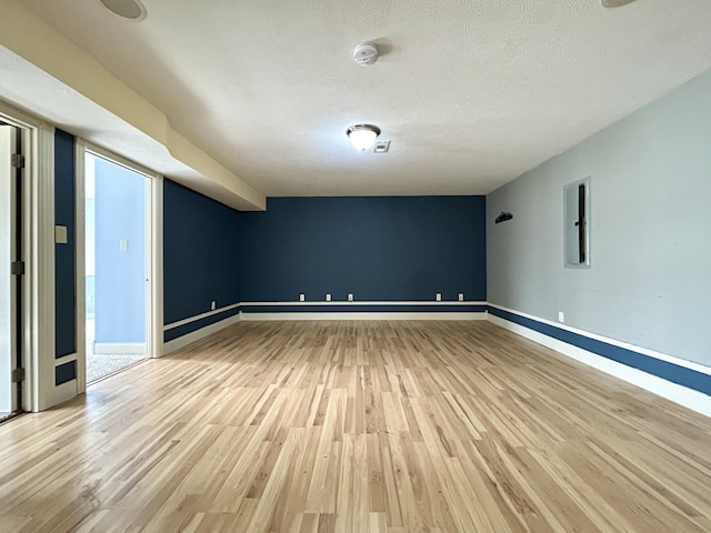 empty room with light wood-style flooring, electric panel, baseboards, and a textured ceiling