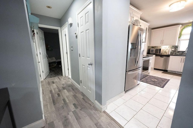 kitchen featuring light tile patterned floors, tasteful backsplash, dark countertops, appliances with stainless steel finishes, and white cabinetry