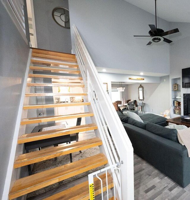 staircase with ceiling fan, wood finished floors, a fireplace, high vaulted ceiling, and recessed lighting