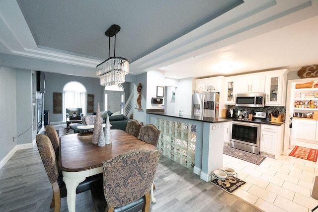 dining room featuring baseboards, light wood-style flooring, stairway, a tray ceiling, and a chandelier