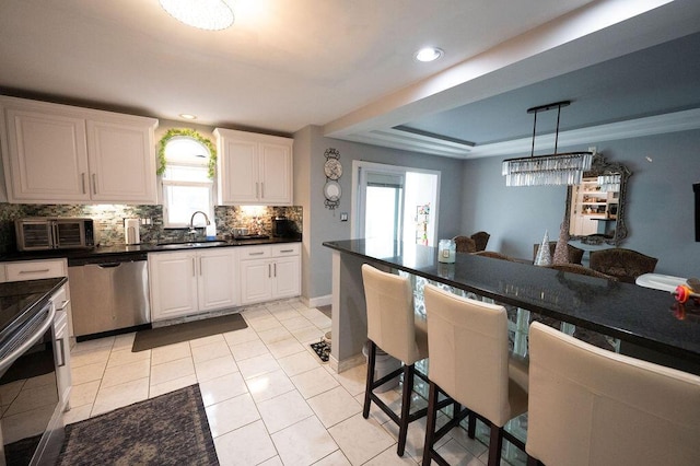 kitchen with a tray ceiling, stainless steel appliances, dark countertops, tasteful backsplash, and a sink