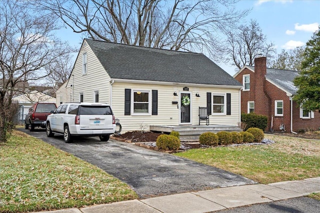 cape cod-style house featuring driveway, a shingled roof, and a front lawn