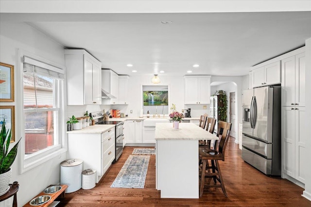 kitchen featuring arched walkways, a breakfast bar area, stainless steel appliances, white cabinets, and a center island