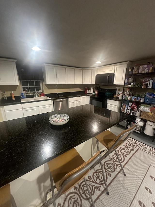 kitchen with black appliances, a kitchen bar, a sink, and white cabinetry