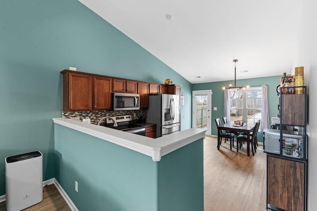 kitchen featuring decorative backsplash, appliances with stainless steel finishes, light wood-style floors, a peninsula, and baseboards