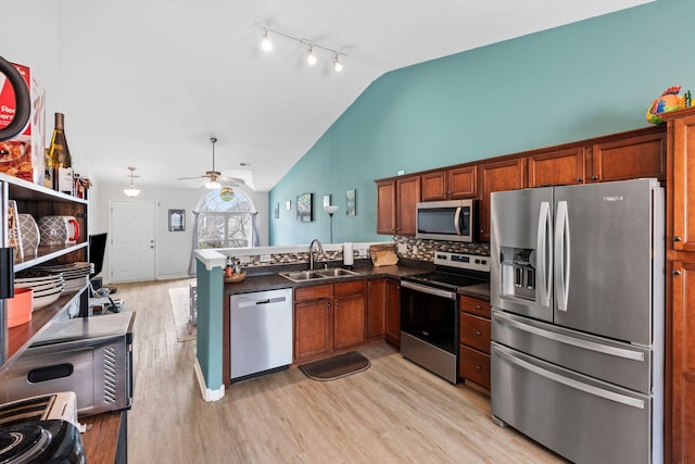 kitchen featuring light wood-style flooring, a peninsula, a sink, appliances with stainless steel finishes, and dark countertops