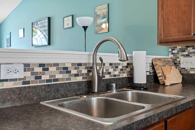 room details with tasteful backsplash, brown cabinetry, dark countertops, and a sink