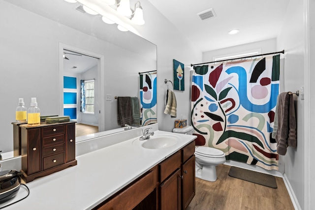 bathroom with toilet, vanity, wood finished floors, and visible vents