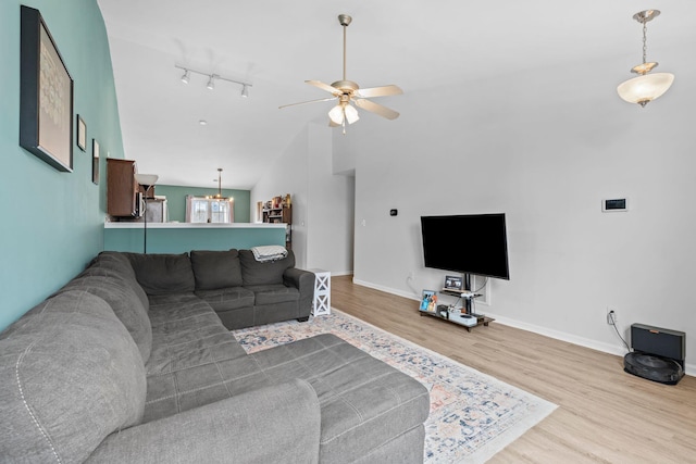 living area featuring ceiling fan with notable chandelier, lofted ceiling, baseboards, and wood finished floors