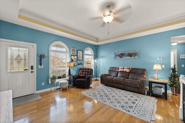 living room featuring wood-type flooring, baseboards, ceiling fan, and crown molding