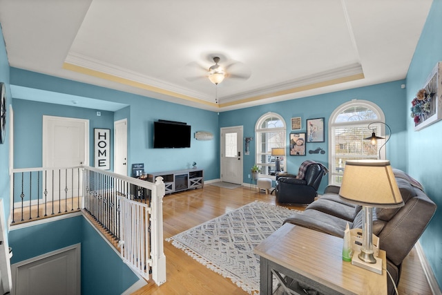 living room featuring a raised ceiling, ceiling fan, baseboards, and wood finished floors