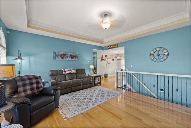 living room featuring ceiling fan with notable chandelier, a raised ceiling, crown molding, and wood finished floors