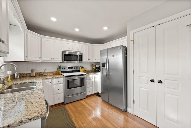 kitchen with light wood finished floors, white cabinetry, stainless steel appliances, and a sink