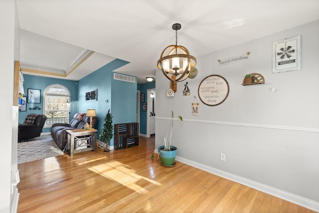 interior space with a chandelier, wood finished floors, visible vents, baseboards, and crown molding