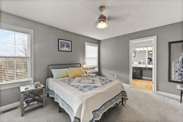 carpeted bedroom featuring a ceiling fan, visible vents, ensuite bath, and baseboards