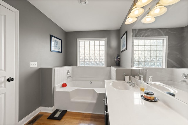 bathroom featuring a garden tub, visible vents, vanity, wood finished floors, and baseboards