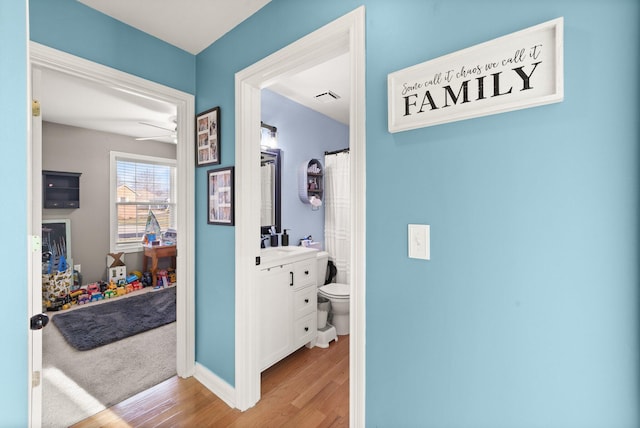 hall with light wood-style floors, baseboards, visible vents, and a sink