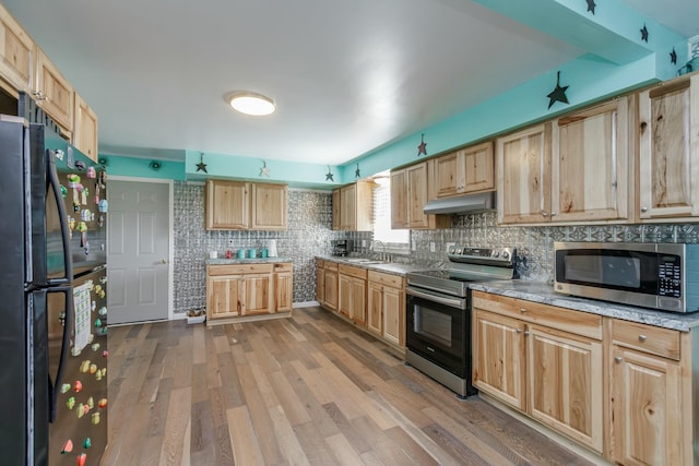 kitchen with appliances with stainless steel finishes, wood finished floors, under cabinet range hood, light brown cabinets, and a sink