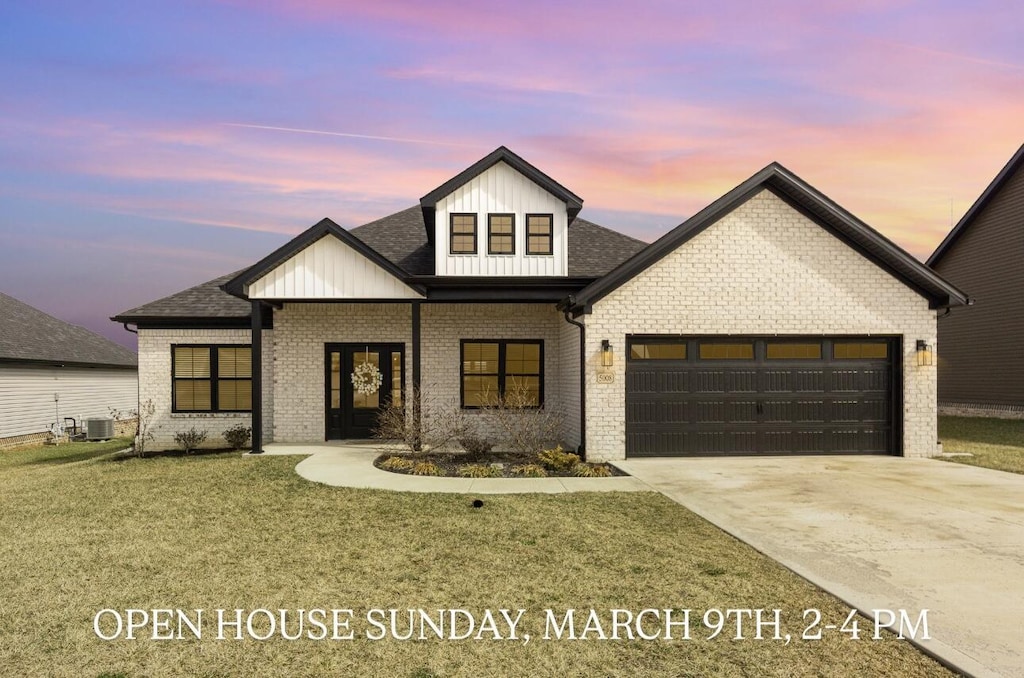 modern farmhouse with a garage, concrete driveway, a yard, central air condition unit, and brick siding