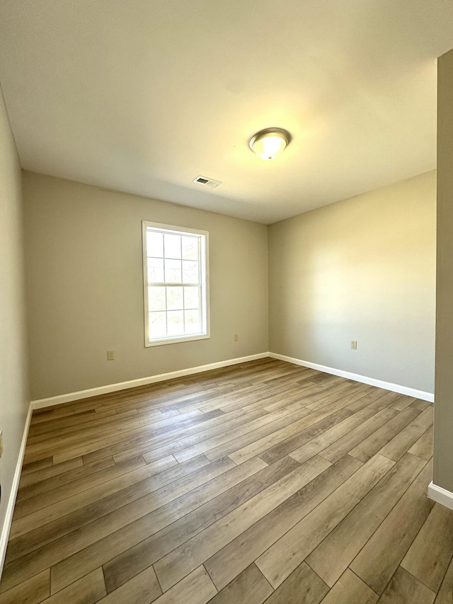 spare room featuring baseboards, visible vents, and wood finished floors