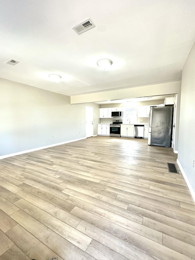 unfurnished living room with light wood-style floors, baseboards, and visible vents