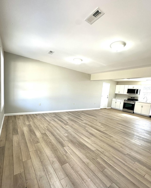 unfurnished living room featuring light wood finished floors, baseboards, and visible vents