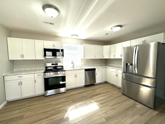 kitchen featuring stainless steel appliances, a sink, white cabinets, light wood-style floors, and light countertops