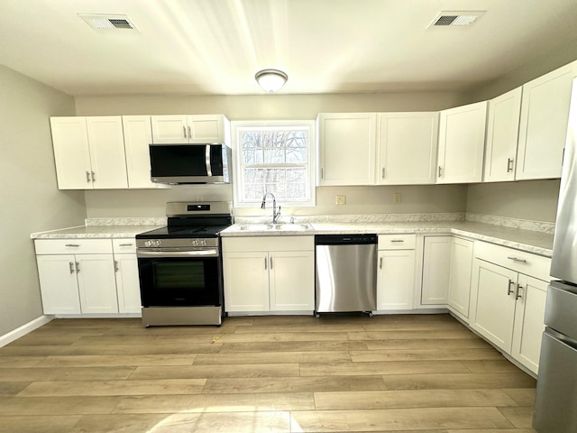 kitchen with stainless steel appliances, light wood-type flooring, white cabinets, and a sink